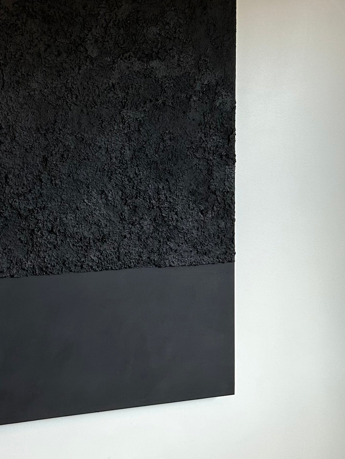 A large black textured wall art canvas hanging on a white wall, with a matte black bottom band and a heavily textured black upper section.